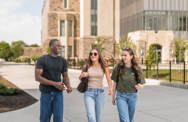 Three friends walking in front of a modern glass building on the Virginia Tech campus