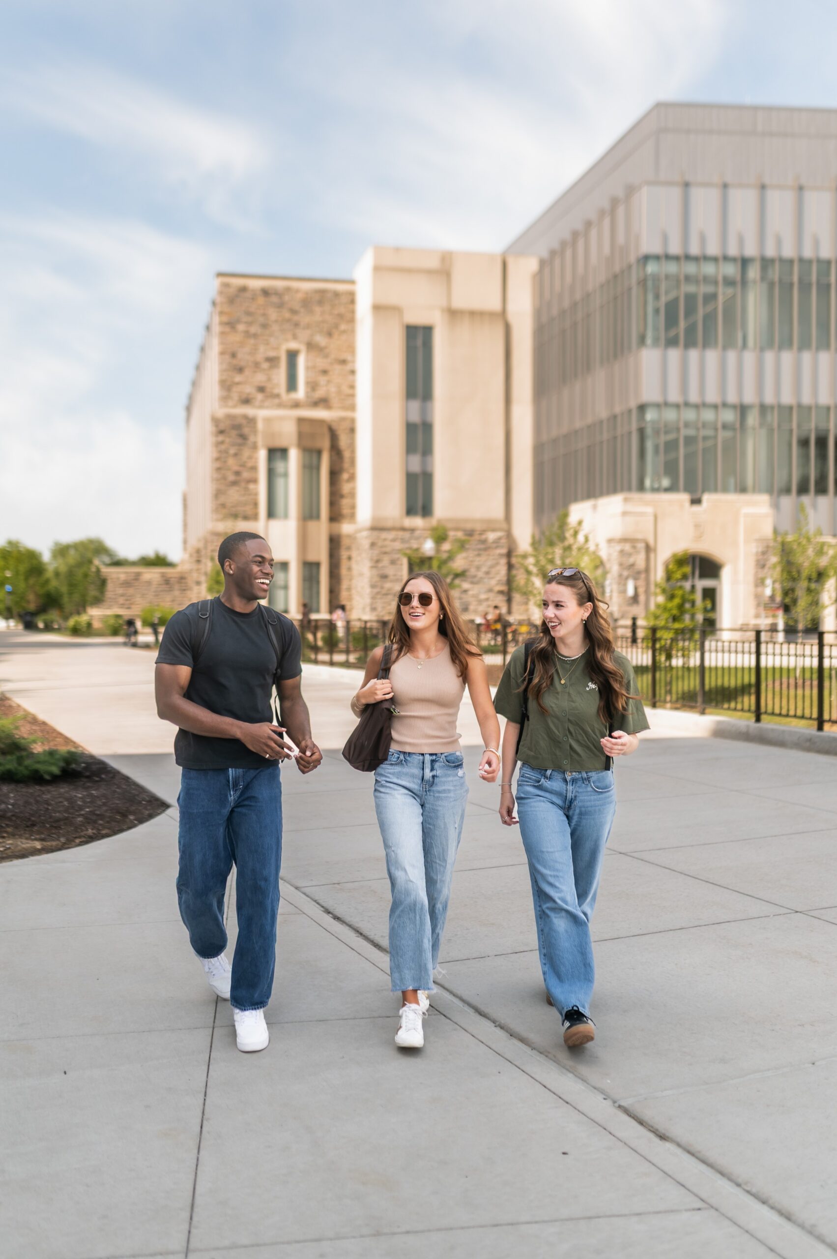 Three friends walking in front of a modern glass building on the Virginia Tech campus scaled