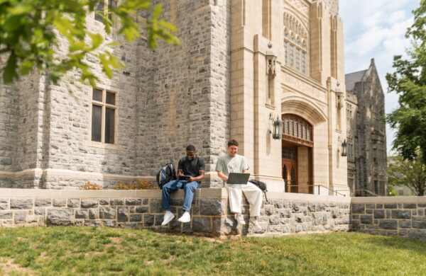Two boys studying sitting on a wall outside a historic campus building